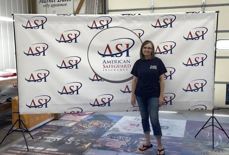 Stacey of Dijohn Designs standing in front of a custom wide-format banner